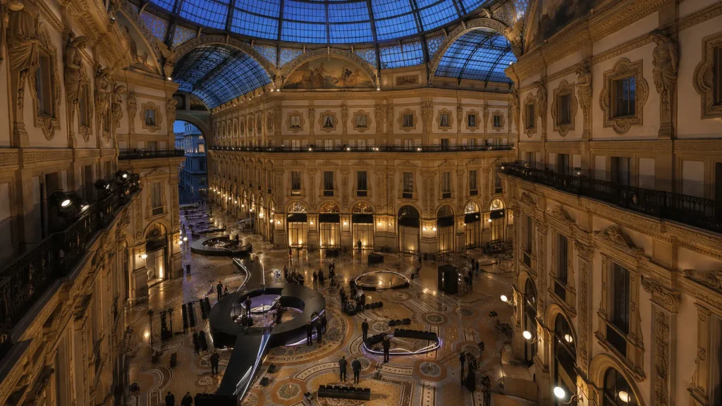 Galleria Vittorio Emanuele II a Milano allestita per una performance di moda, con passerella, tecnici e ospiti sotto la cupola illuminata.