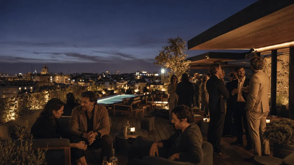 Rooftop di un private members club a Milano al tramonto, con piscina, skyline cittadino e gruppi di professionisti in conversazione.