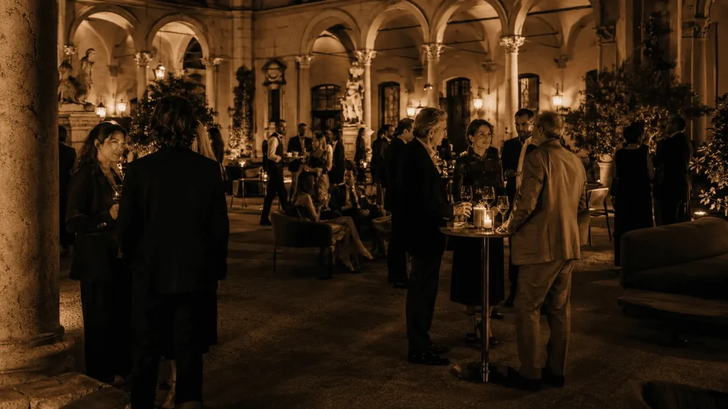 Cortile rinascimentale di un private members club a Roma durante un elegante evento serale, con ospiti in conversazione, luci calde e atmosfera esclusiva.